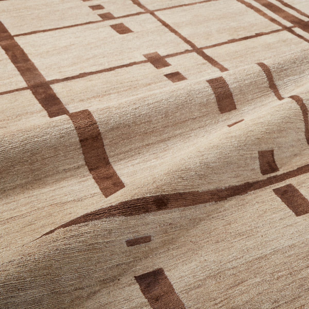 A close-up of a textured area rug with a modern geometric pattern in dark brown on a warm beige background.