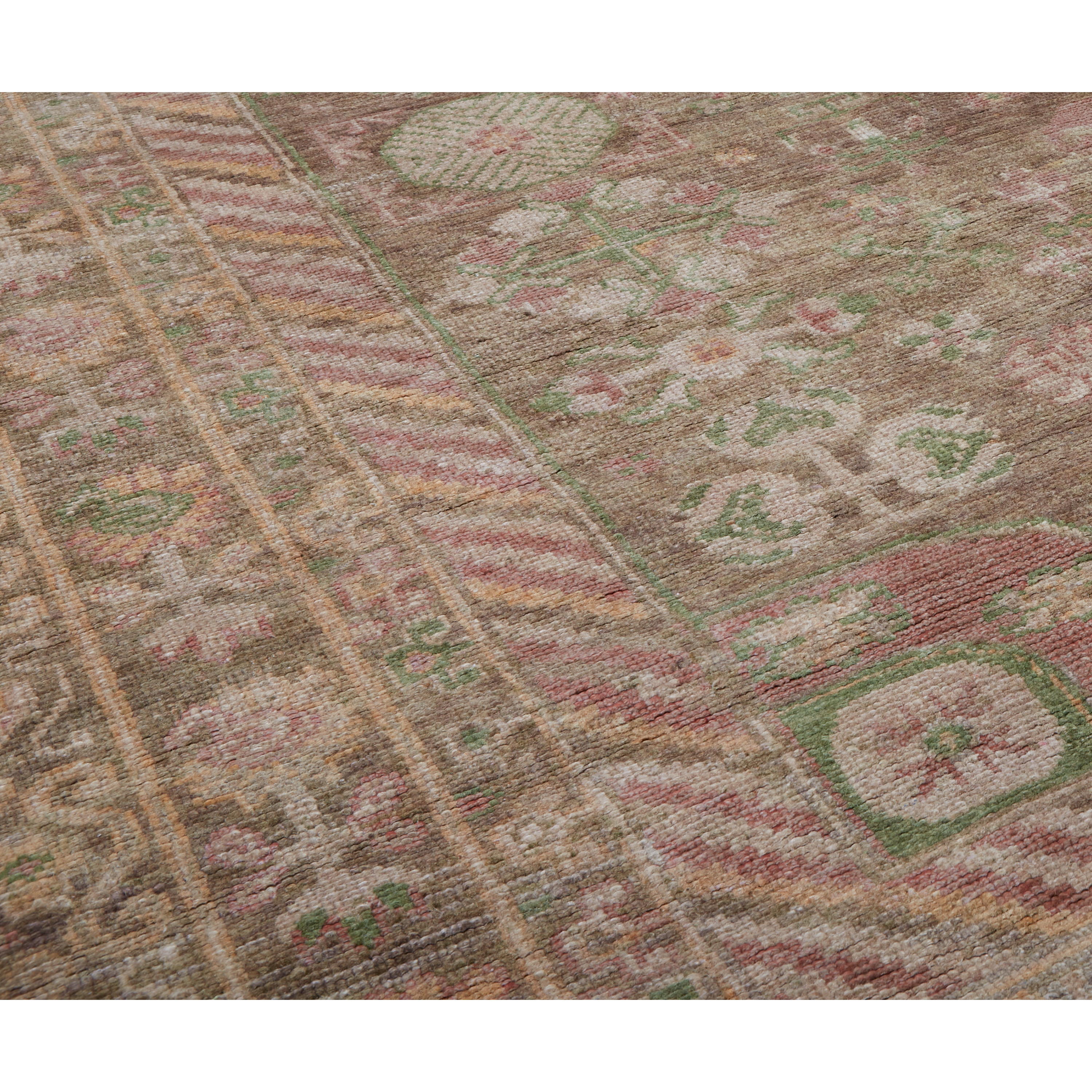 A close-up view of a traditional patterned rug with a warm brown base, featuring intricate floral motifs in muted pink, sage green, and cream.