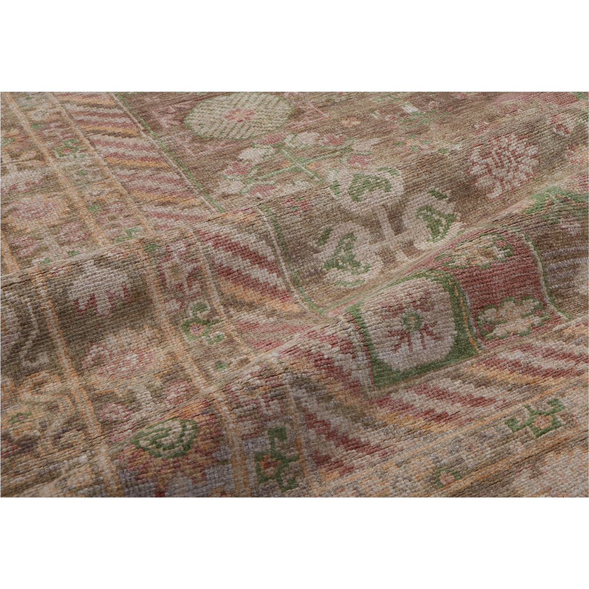 A close-up of a vintage-style area rug with a distressed tribal pattern in muted tones of brown, beige, dusty red, and sage green.