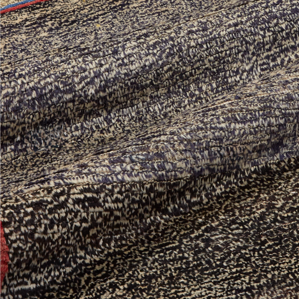 A close-up of a textured woven fabric with a mottled pattern of black, beige, and gray threads, draped to show its texture and weave.