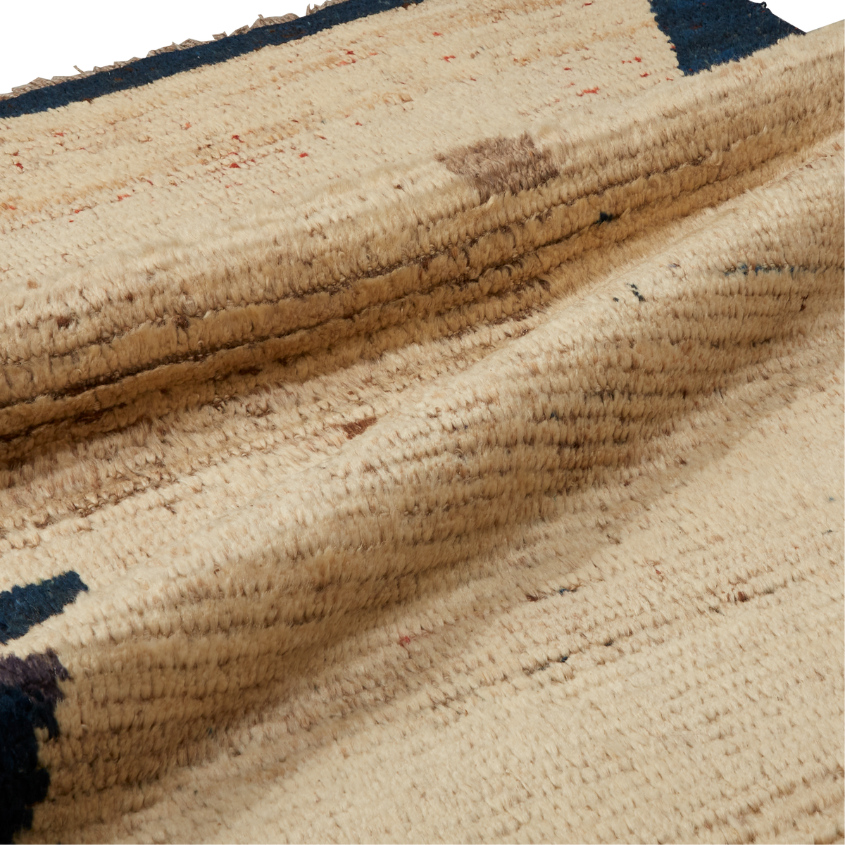 A close-up of a textured woven rug in natural beige with dark navy blue geometric accents and subtle brown and orange flecks.