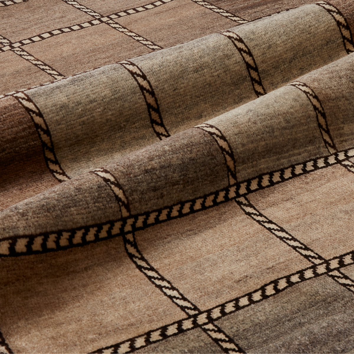 A close-up of a woven textile or rug with a brown and beige plaid pattern, showing the fabric texture and folds.