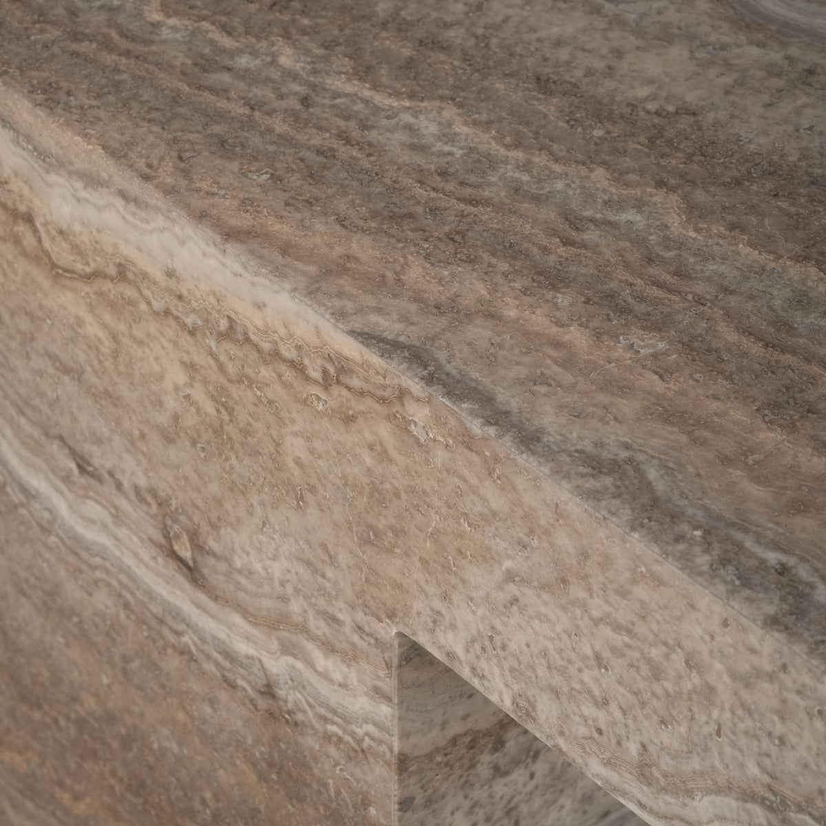 Close-up of the top edge and leg of the Duvall Console Table in Taupe travertine, showing the grey honed top meeting the sandier side face, with wavy tan banding and the open space between the legs below.