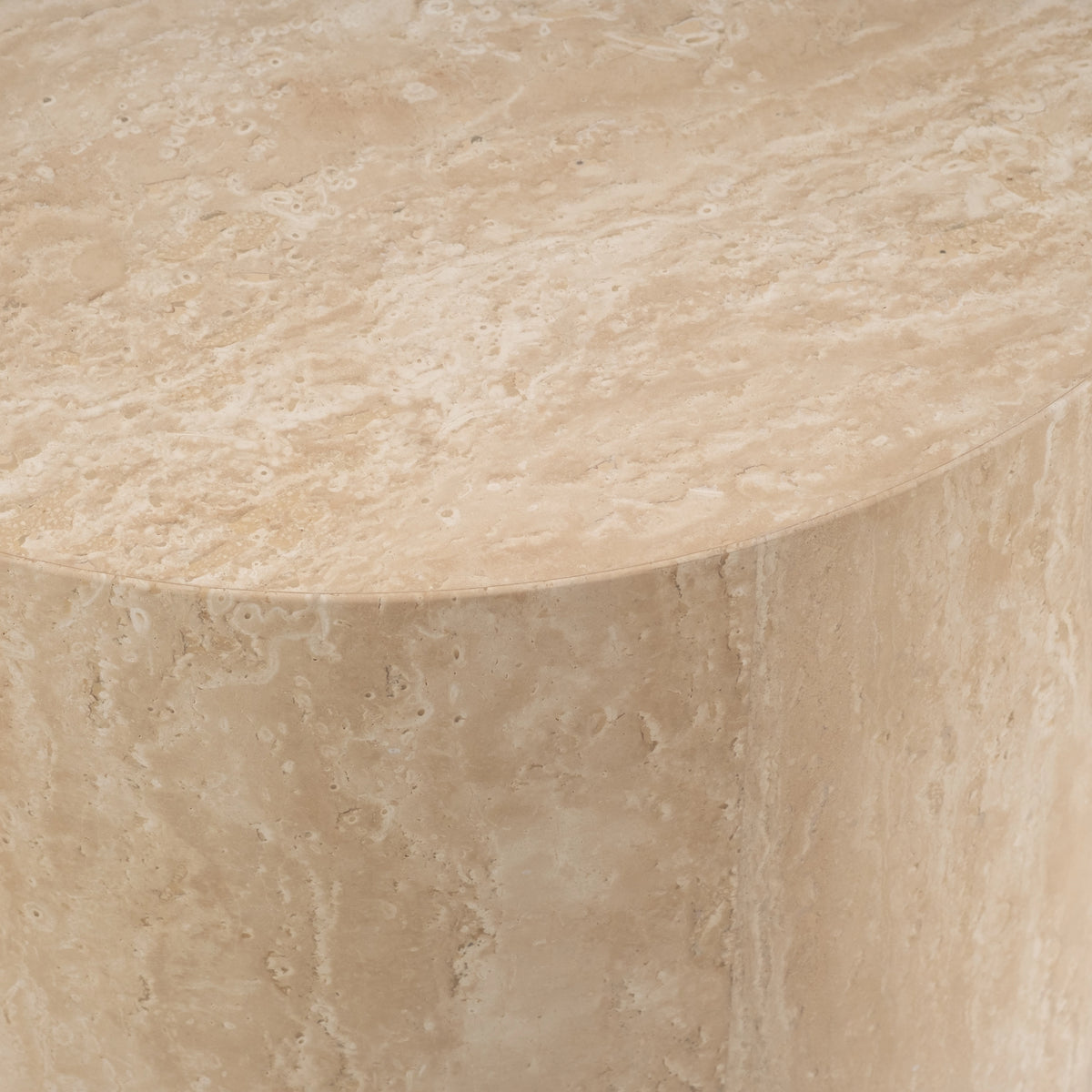 Close-up showing the rim of the Meta Round Side Table in Warm Beige travertine, where the honed top meets the curved side, with natural pitting and soft vertical veining.