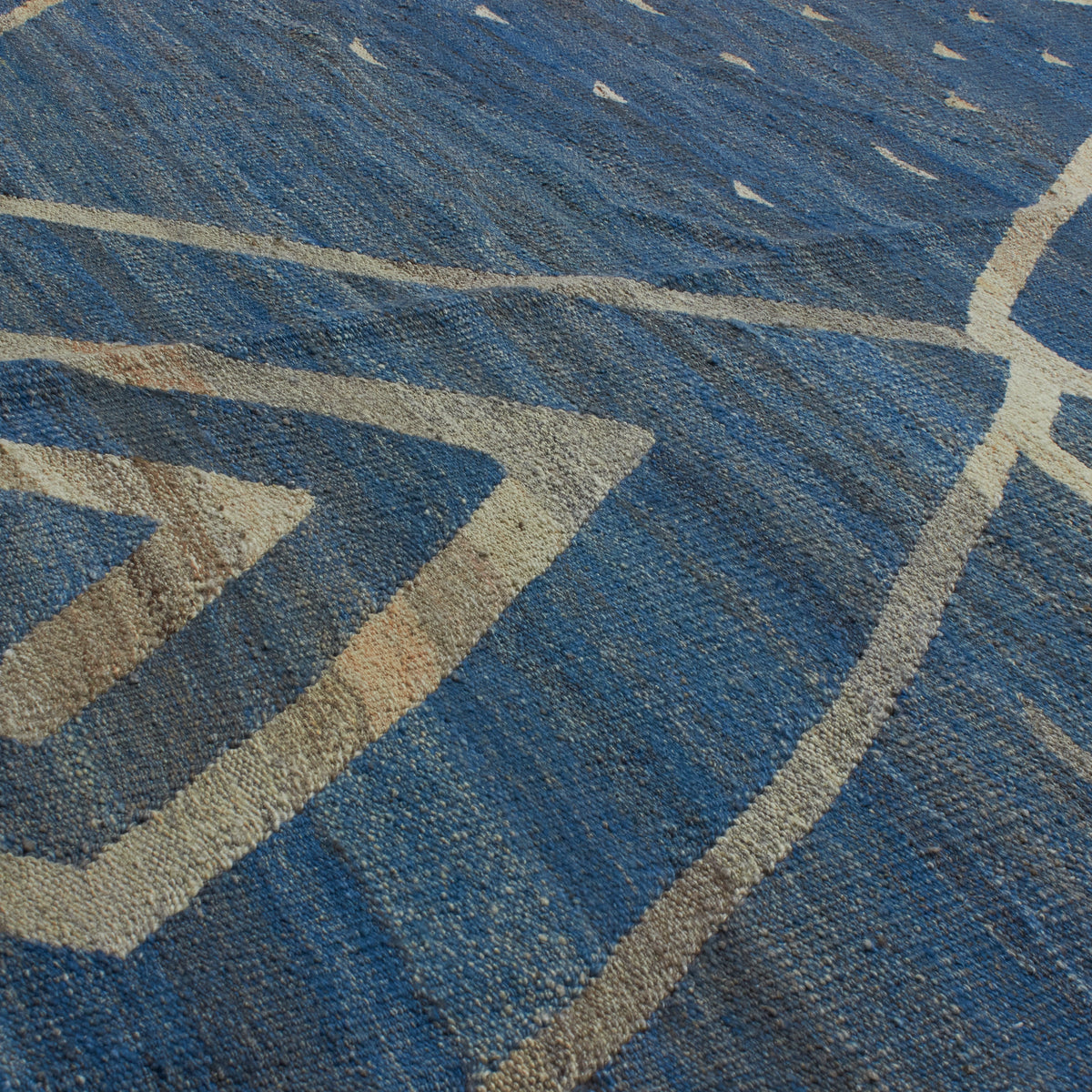 A close-up of a blue woven rug with a geometric pattern in beige and white.