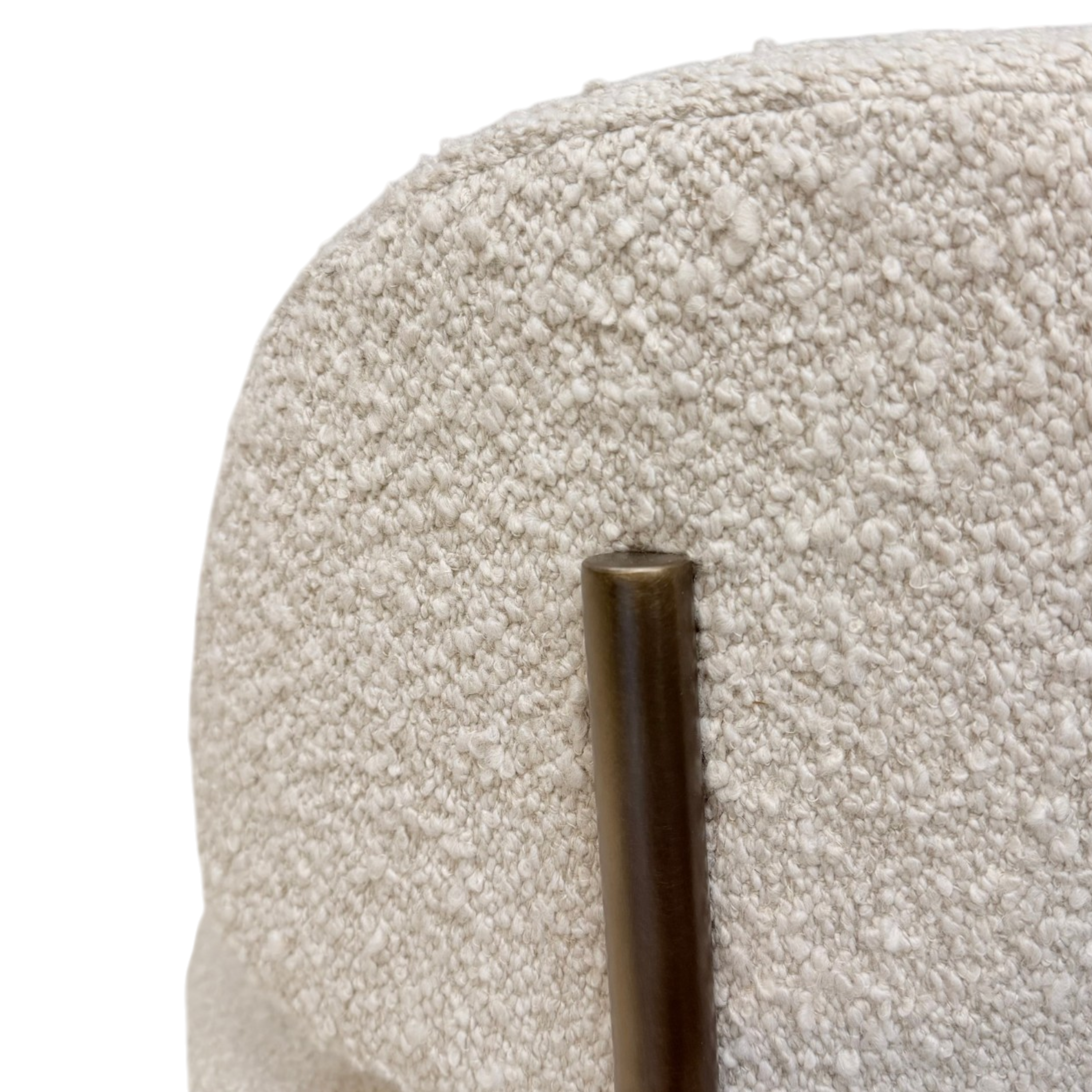 Close-up detail of a textured cream bouclé upholstered chair back with a vertical bronze metal support rod.