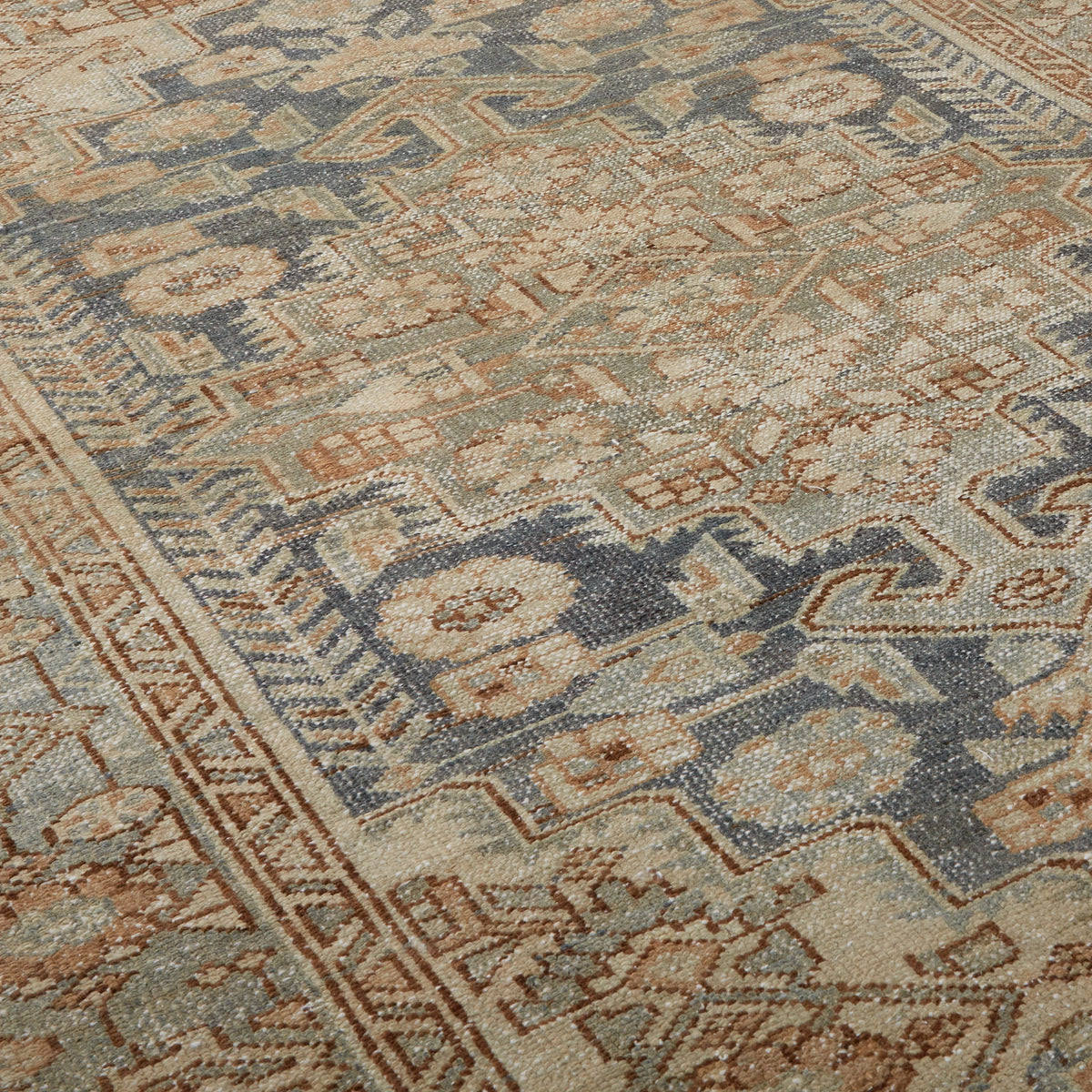 A close-up of a traditional patterned rug with a geometric and floral design in muted blue, beige, and rust brown tones.