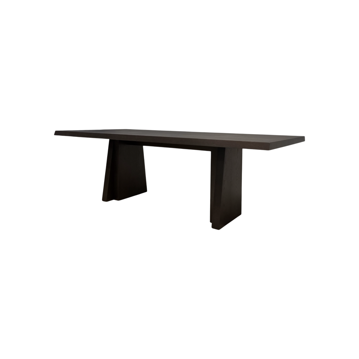 Angled view of the Oblique Dining Table showing its elongated dark wood top, chamfered edges and sculptural splayed pedestal bases.