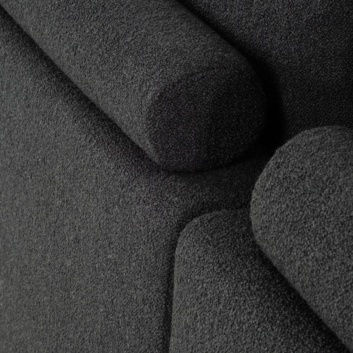 Detail shot of the Colonna Modular Sectional in charcoal bouclé, with a rounded bolster, the stitched back cushion, and the softly padded arm shown together.