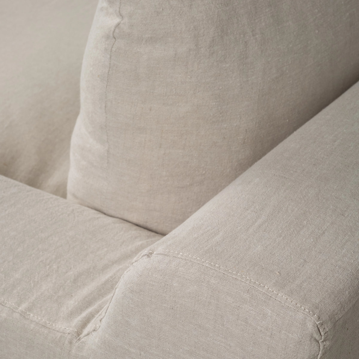 Detail of the Babylon Sofa in natural linen, showing the relaxed seat cushion, back cushion and the topstitched arm.
