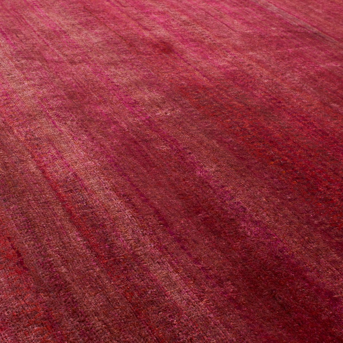 A close-up of a textured rug or fabric in a rich magenta and deep red tone with subtle tonal variation and a distressed, vintage finish.