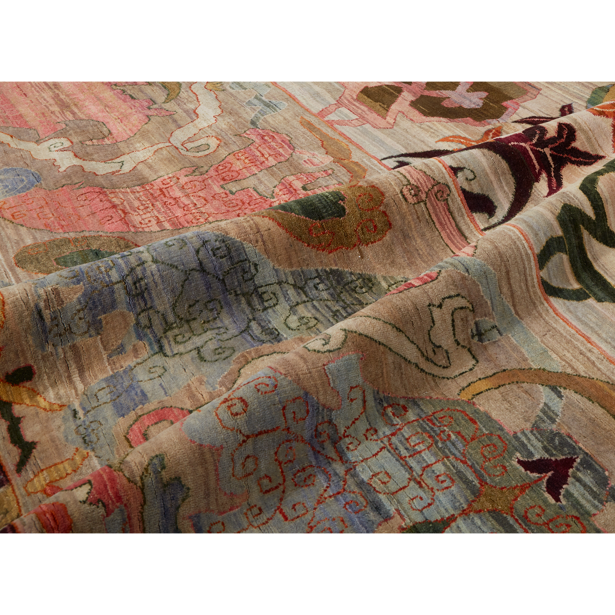 A close-up of a folded area rug with an intricate, vintage-style multicolor pattern featuring shades of beige, pink, blue, green, and brown.