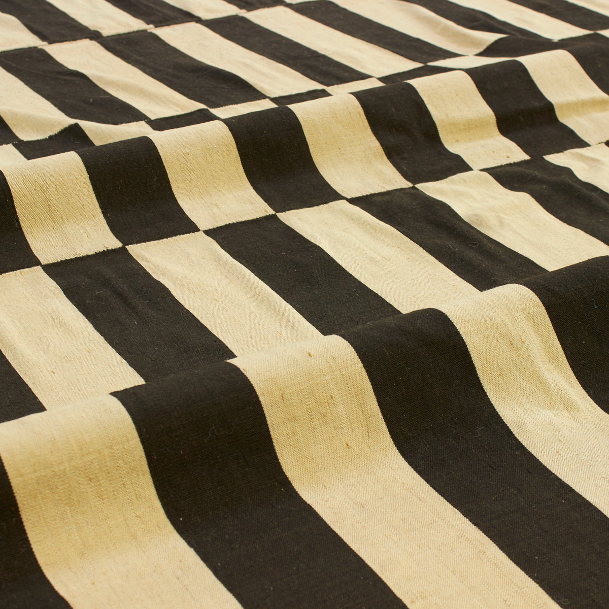 A close-up of a woven fabric with bold, alternating black and natural beige stripes in a diagonal pattern.