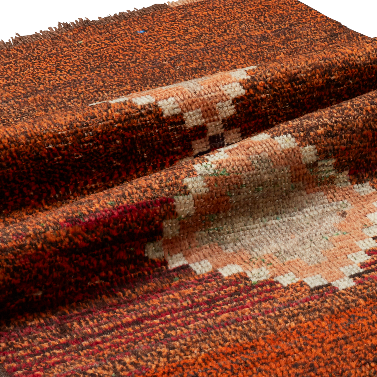 A close-up of a textured woven rug with a Southwestern geometric pattern in rust orange, terracotta, beige, and dark brown.