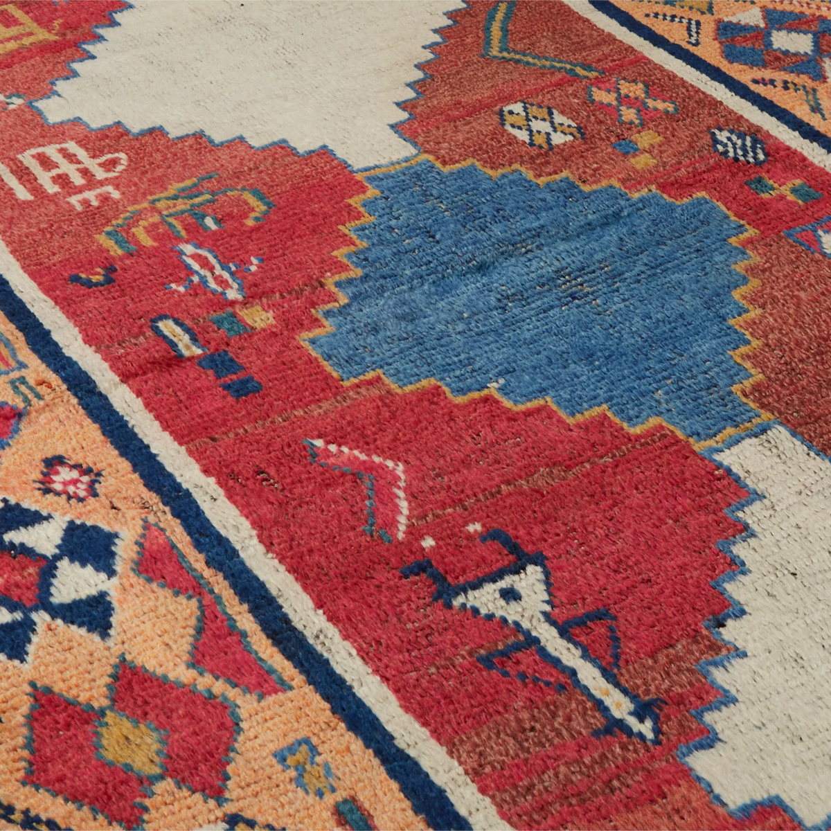 Close-up of a woven rug with a geometric pattern in red, blue, cream, and orange tones.