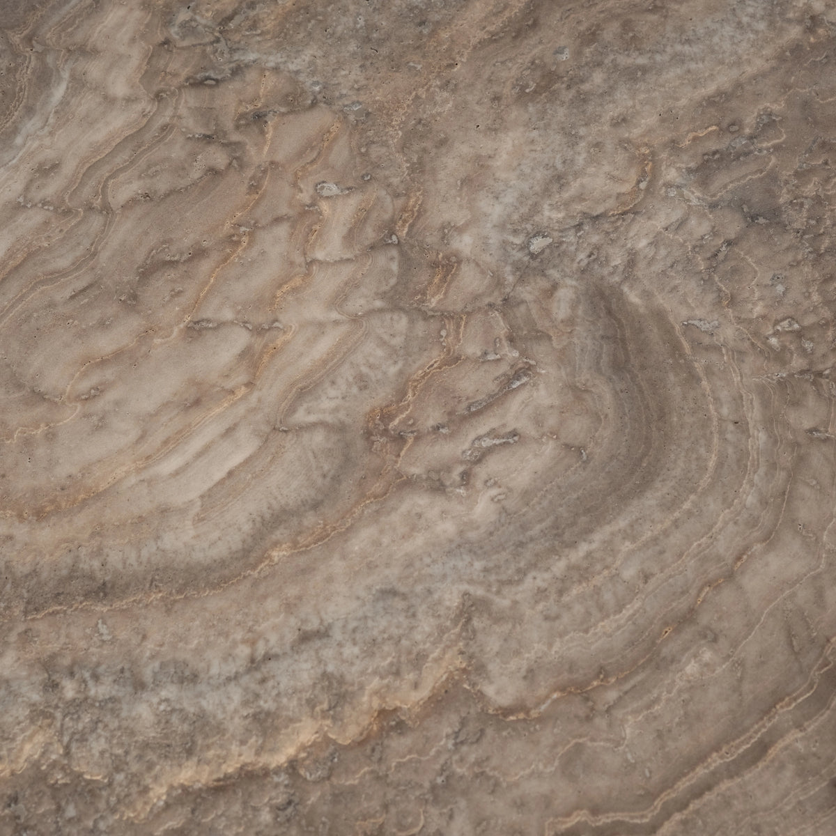 Close-up showing the layered surface of the Duvall Console Table in Taupe travertine, with curving cream and tan bands, fine pitting, and soft grey-brown mottling across the honed face.