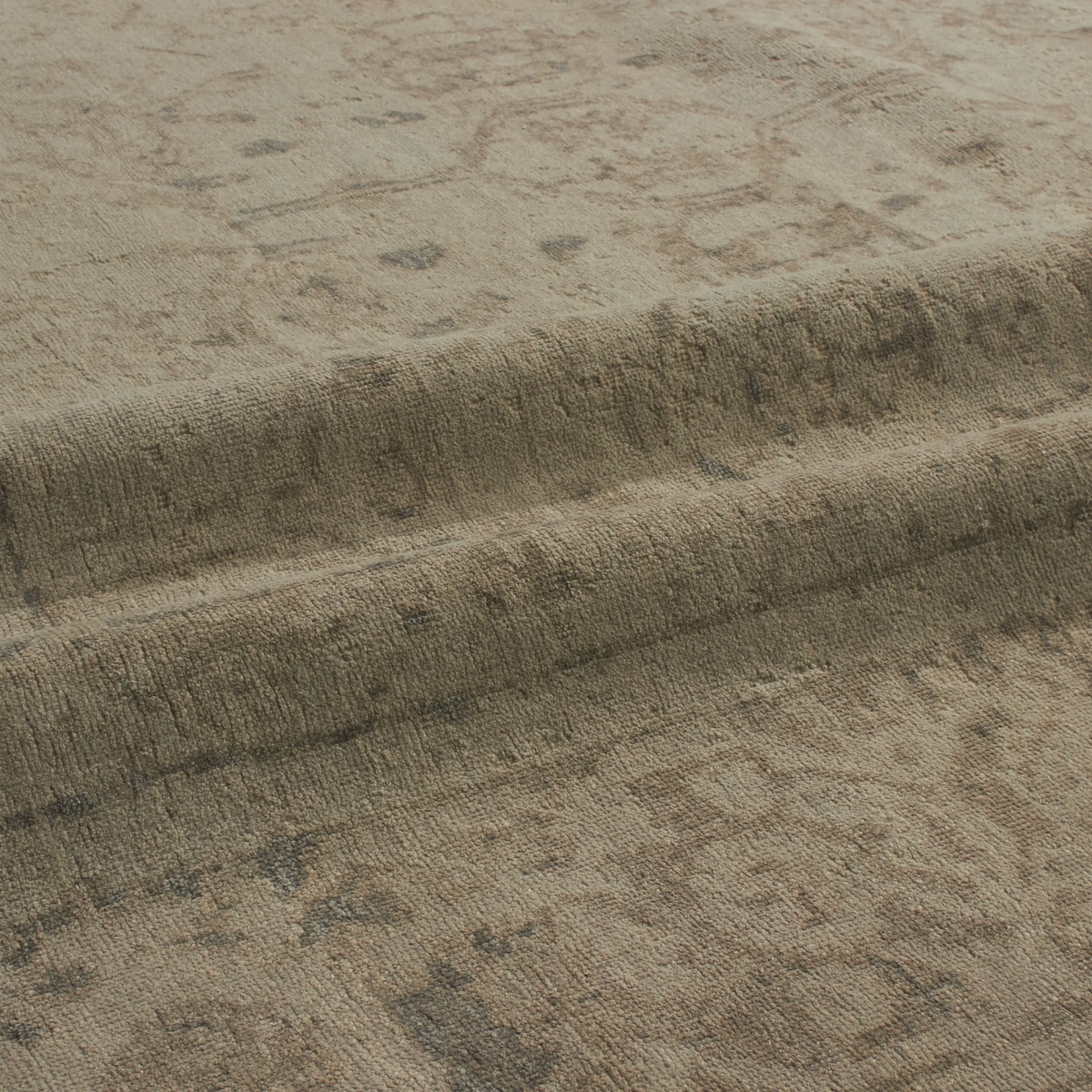 Close-up of a textured area rug in a warm taupe-beige color with a subtle distressed traditional pattern.