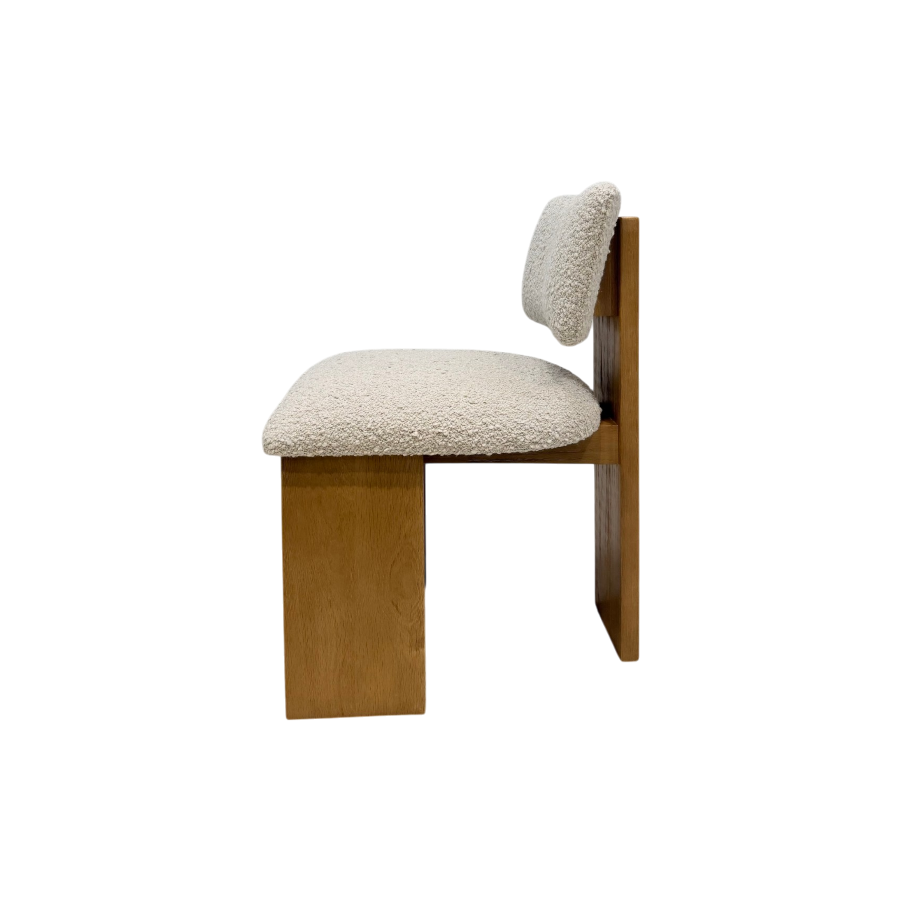 A mid-century modern wooden chair with a chunky block seat and back, upholstered in a textured cream bouclé fabric, shown from a side profile on a white background.