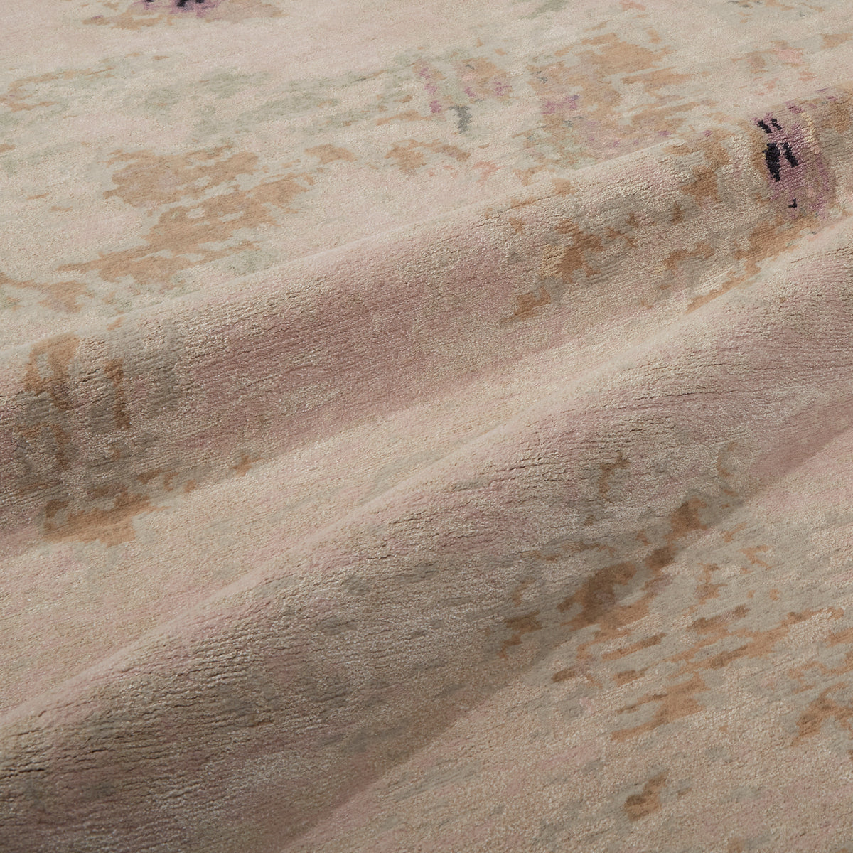 A close-up of a plush area rug with a distressed, vintage-inspired pattern in dusty pink, beige, and muted brown tones.