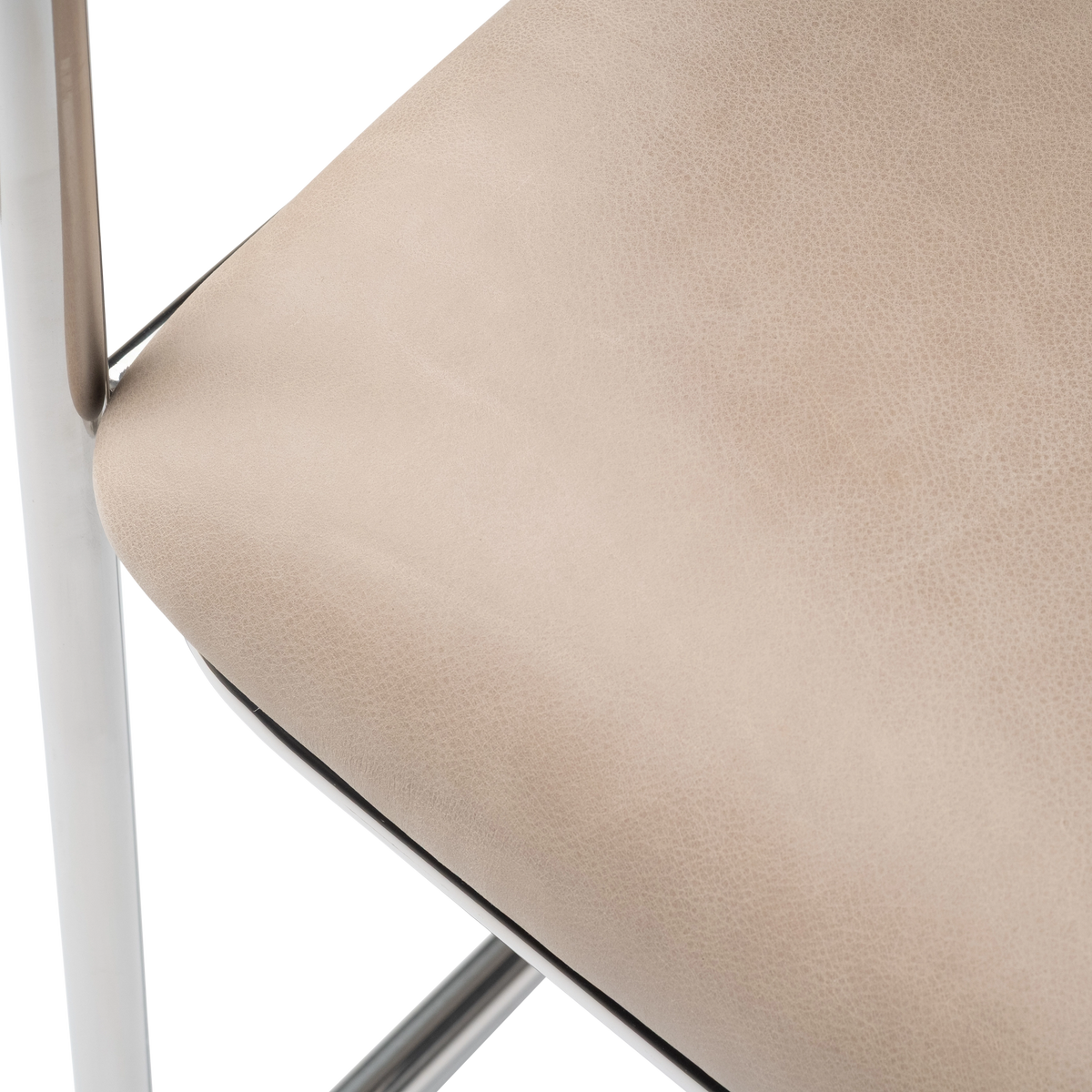 Close-up showing the seat of the Rhodes Arm Chair in taupe top grain leather, with fine pebbled grain, a rounded front edge, and the polished steel frame beside it.