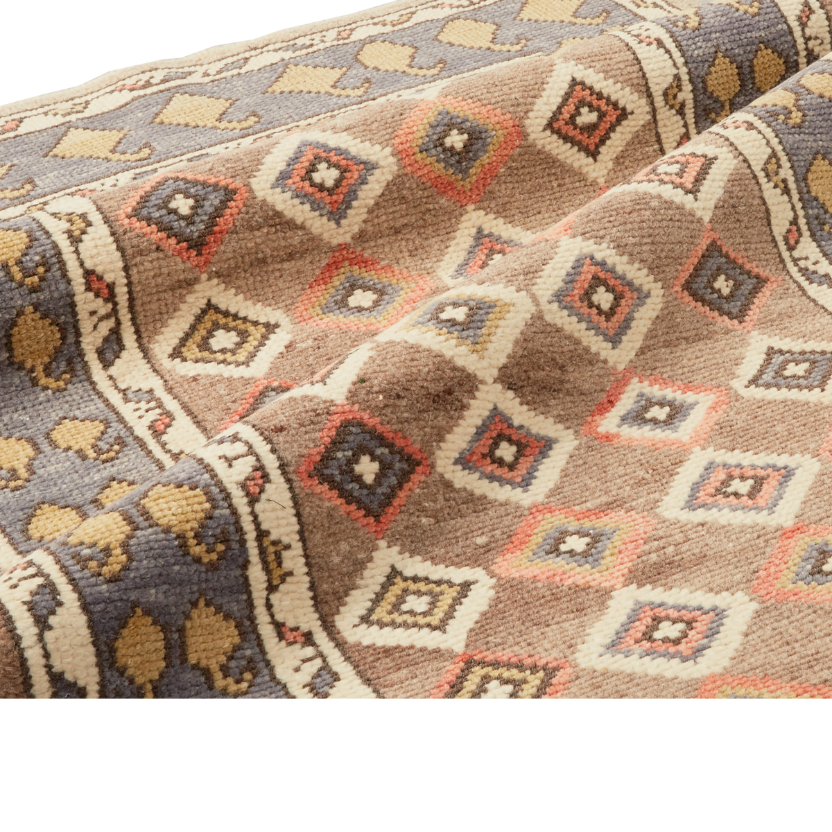 A close-up of a woven textile with a geometric diamond pattern in beige, brown, cream, muted blue-gray, and coral-red, draped to show texture and fold detail.