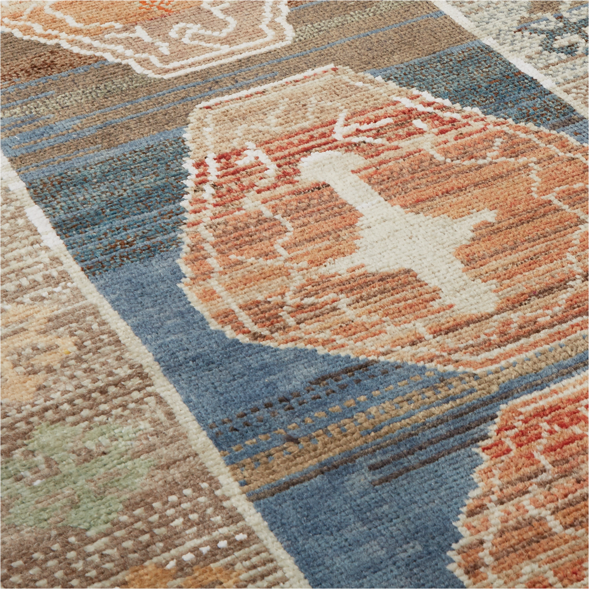 A close-up of a textured area rug with a geometric tribal pattern in shades of blue, terracotta, beige, and white.
