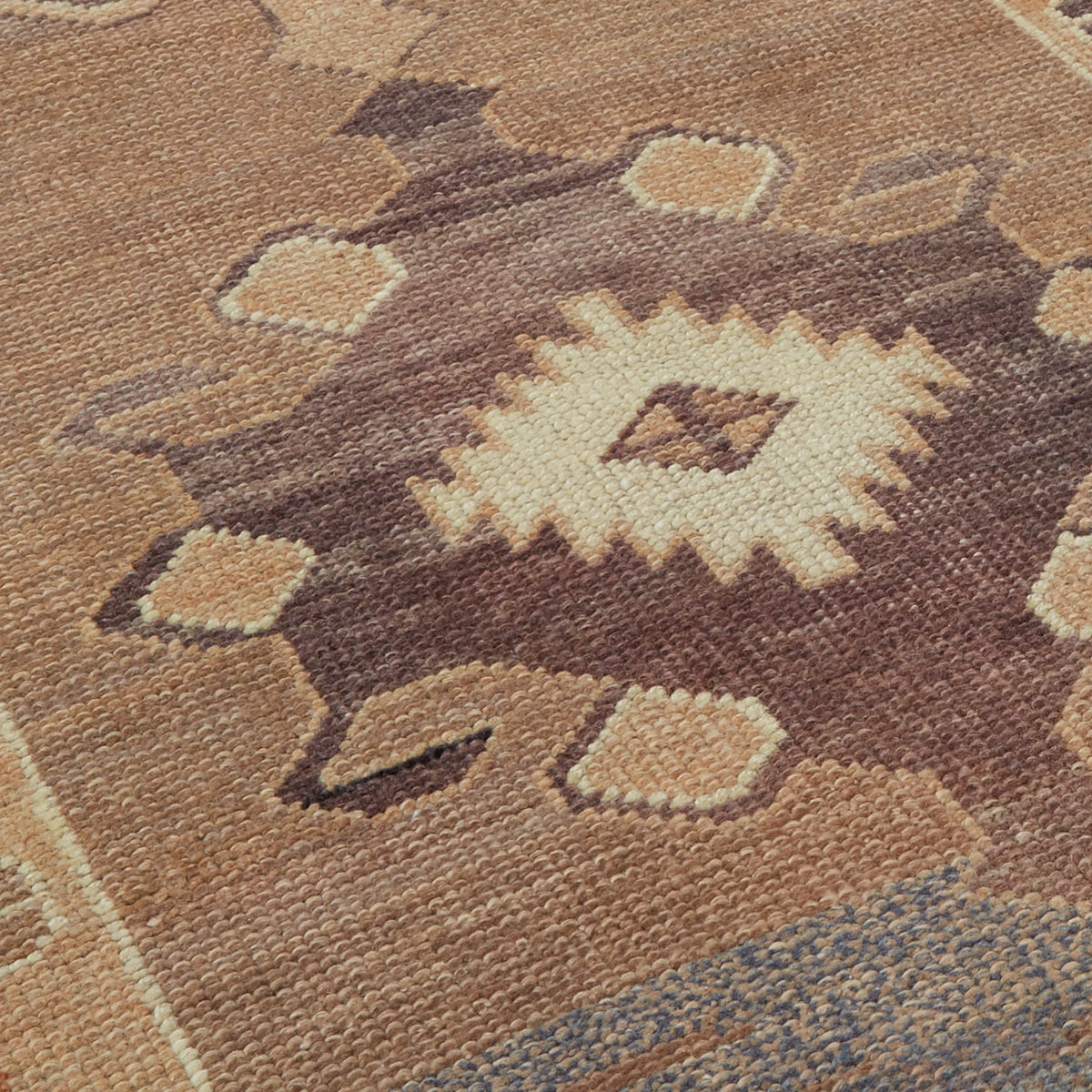 Close-up of a woven rug with a geometric Southwestern-style pattern in earthy tones of brown, beige, and muted blue.